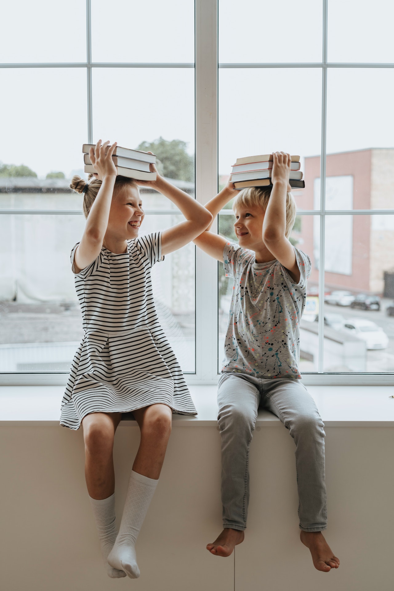 2 children sitting in a window with books on their head, preparing for a kids IQ test. 